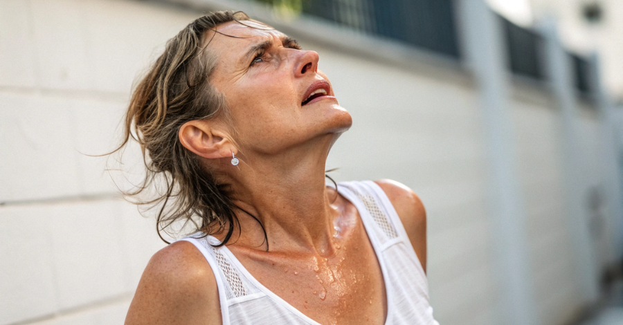 Mulher suando intensamente ao ar livre, com expressão de desconforto e cabelo molhado, representando um episódio de fogacho causado pela menopausa