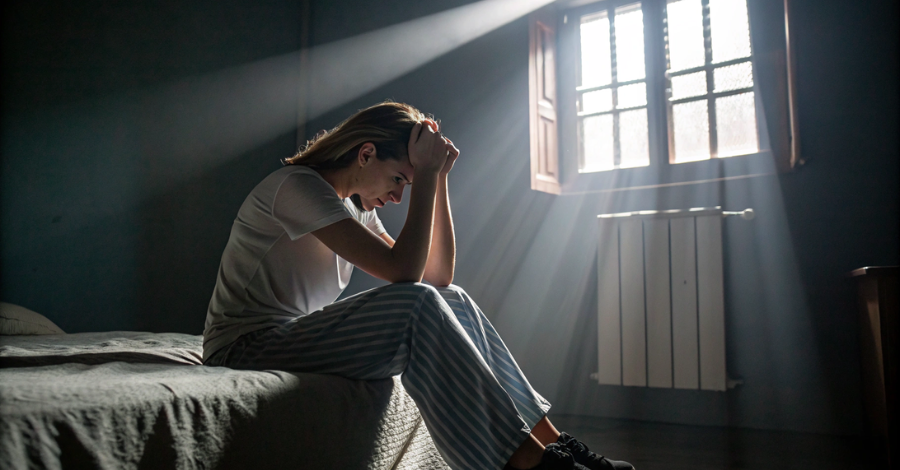 Mulher sentada na cama, segurando a cabeça, representando a frustração dos sintomas da menopausa precoce